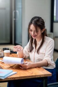 Happy young Asian businesswoman holding documents deciding if startup loan vs business credit card is better.